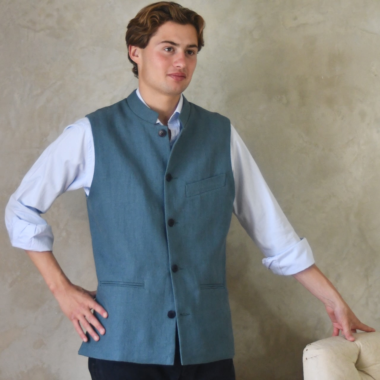 Light blue Slim cut linen gilet from Weskit. Handmade in London, this slubby linen waistcoat is made in pure Irish linen and lined in striped cotton ticking. Mandarin collar and Courtney and Co buttons. Entirely made in Great Britain. Buttoned View.