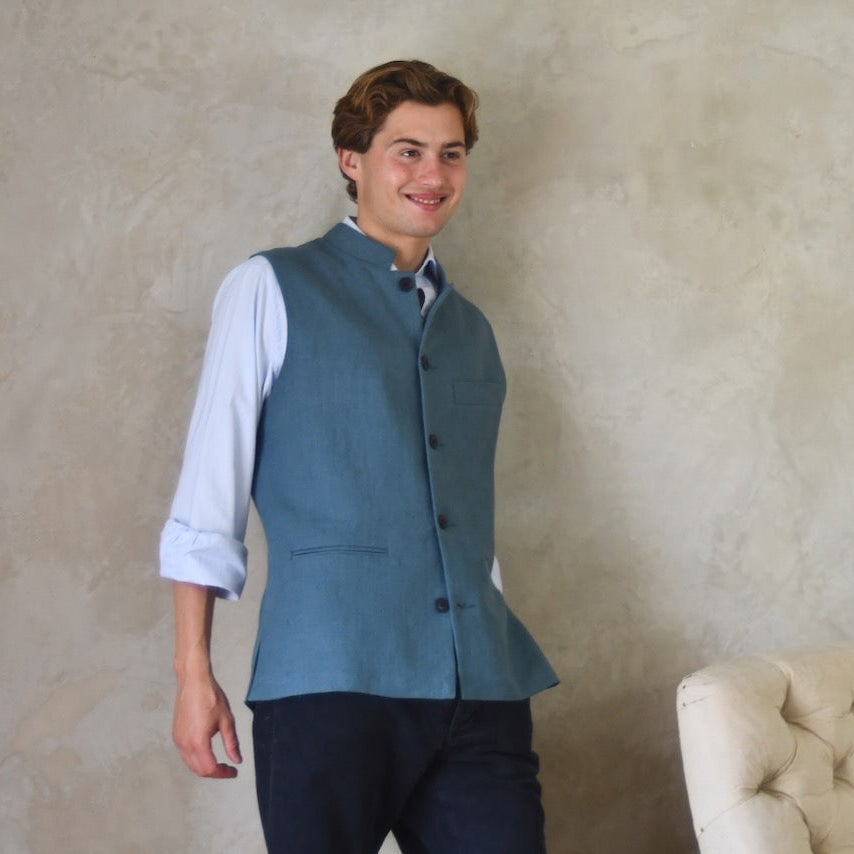 Light blue Slim cut linen gilet from Weskit. Handmade in London, this slubby linen waistcoat is made in pure Irish linen and lined in striped cotton ticking. Mandarin collar and Courtney and Co buttons. Entirely made in Great Britain. Buttoned Side View.