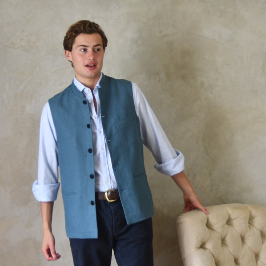 Light blue loose cut linen gilet from Weskit. Handmade in London, this slubby linen waistcoat is made in pure Irish linen and lined in striped cotton ticking. Mandarin collar and Courtney and Co buttons. Entirely made in Great Britain. Worn Open.