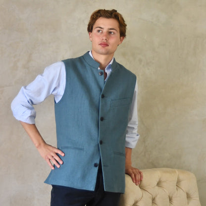 Light blue loose cut linen gilet from Weskit. Handmade in London, this slubby linen waistcoat is made in pure Irish linen and lined in striped cotton ticking. Mandarin collar and Courtney and Co buttons. Entirely made in Great Britain. Closed View.