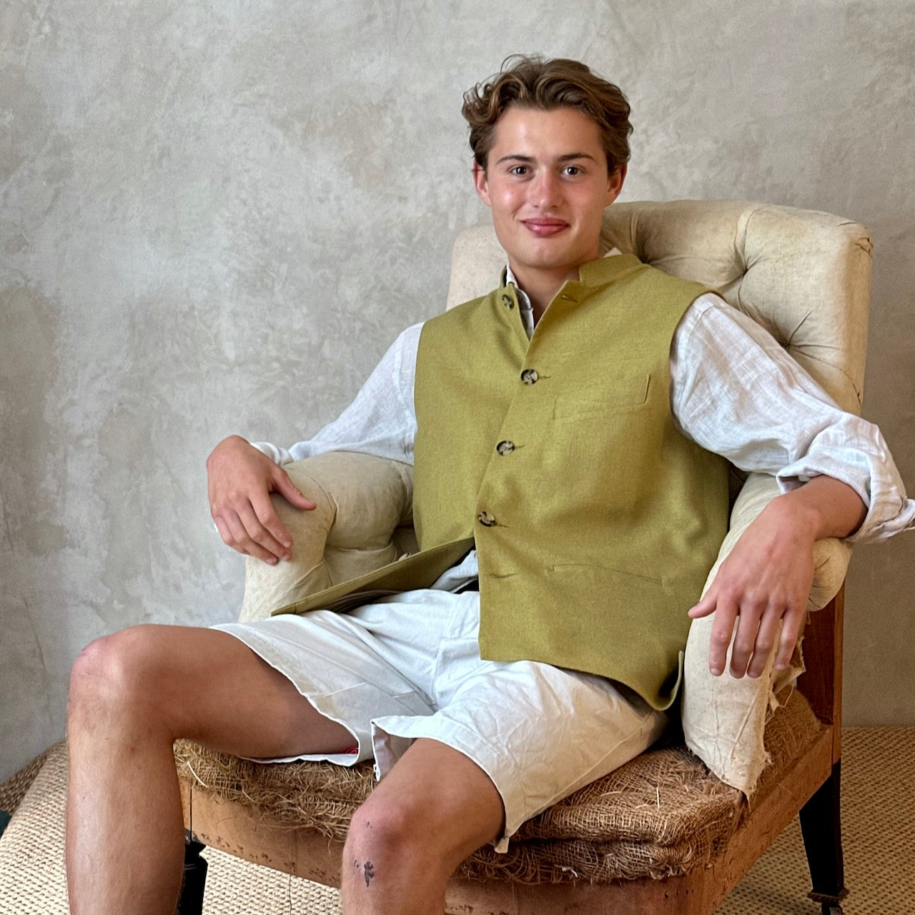 Relaxed fit summer weight gilet in green silk weave. Handmade in London this gilet has a Mandarin collar and is fully lined in pure cotton ticking. Made in Great Britain. Seated shot.