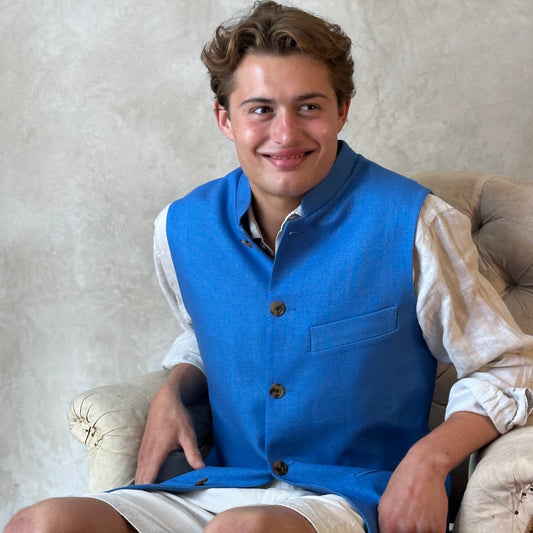 Slim fit gilet in sky blue summer weight silk weave. Handmade in London this fitted waistcoat has five pockets and a Nehru collar. Made in Great Britain. Seated Modelled Shot.