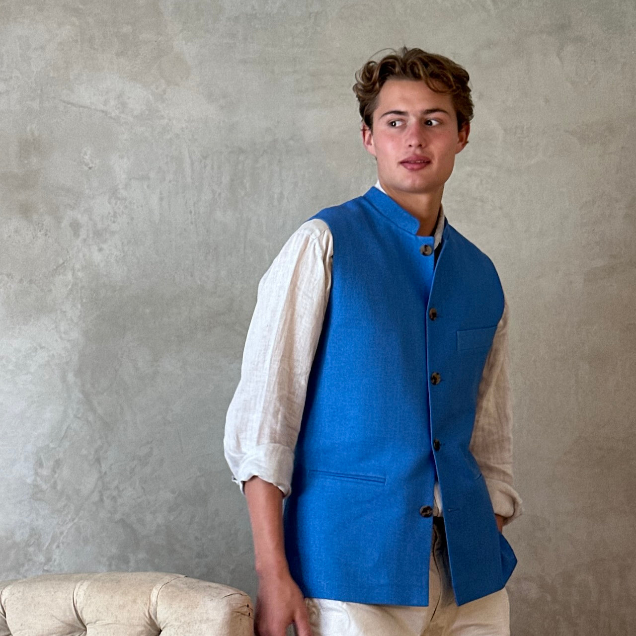 Slim fit gilet in sky blue summer weight silk weave. Handmade in London this fitted waistcoat has five pockets and a Nehru collar. Made in Great Britain. Standing side shot.