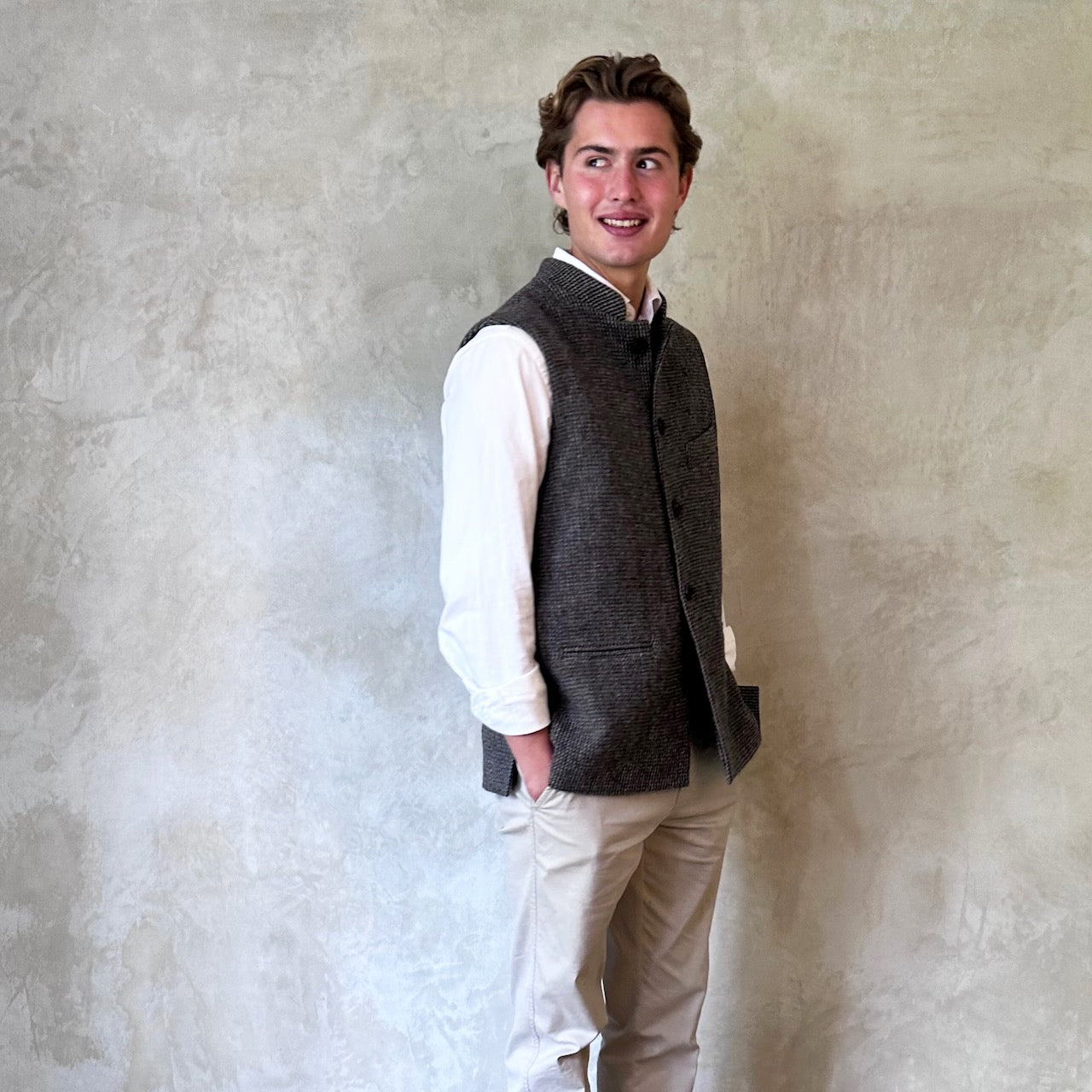 Warm Nehru Style Gilet in pure wool tweed from Hawick. Handmade in London this waistcoat has a gentle patterning in blue and shades of taupe and grey. Ample pocket space, side vents and a nead Mandarin Collar. Side View.