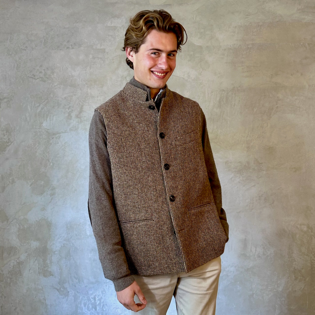 A wonderfully warm Nehru-style gilet in a thick tweed from Hawick. Designed in Wales, oven in England, handmade in London with buttons from Gloucestershire, this is a truly British Waistcoat. Detail Shot. Side vents for ease and five pockets for storage! Buttoned Smiling Shot.