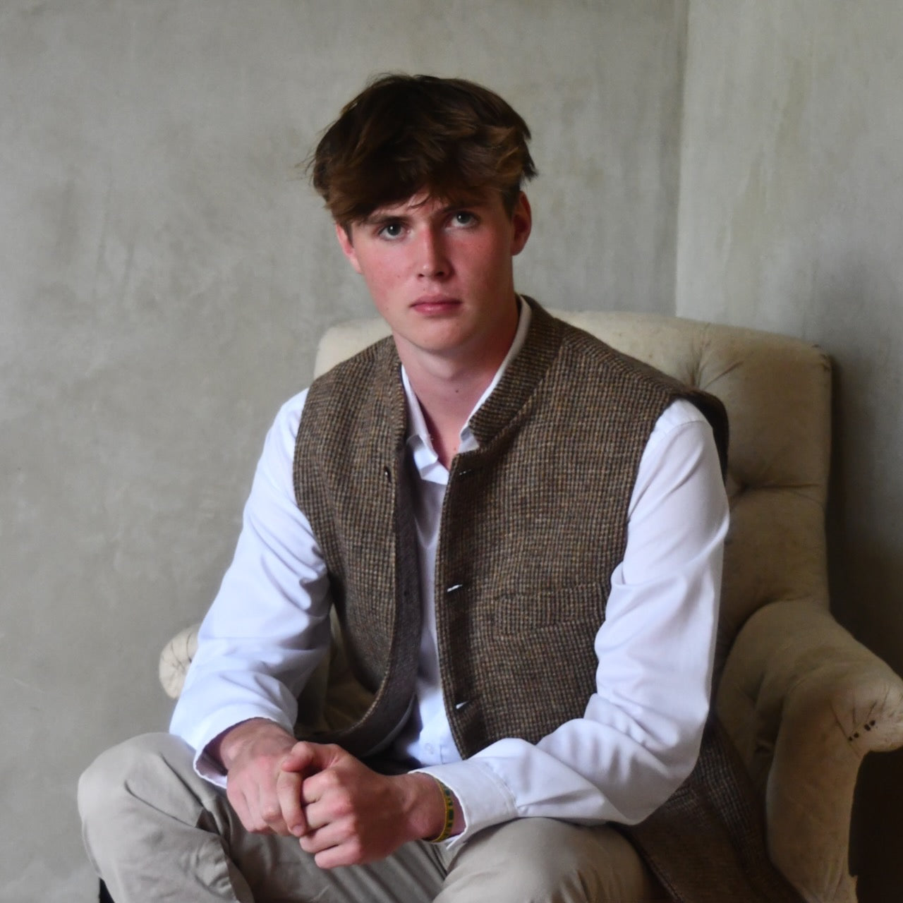 Seated View of Bespoke Nehru Style Gilet in Brown Patterned Pure Wool Tweed. This tweed from Lovat Mill has a delicate patterning. Shown over a white shirt with Chinos.