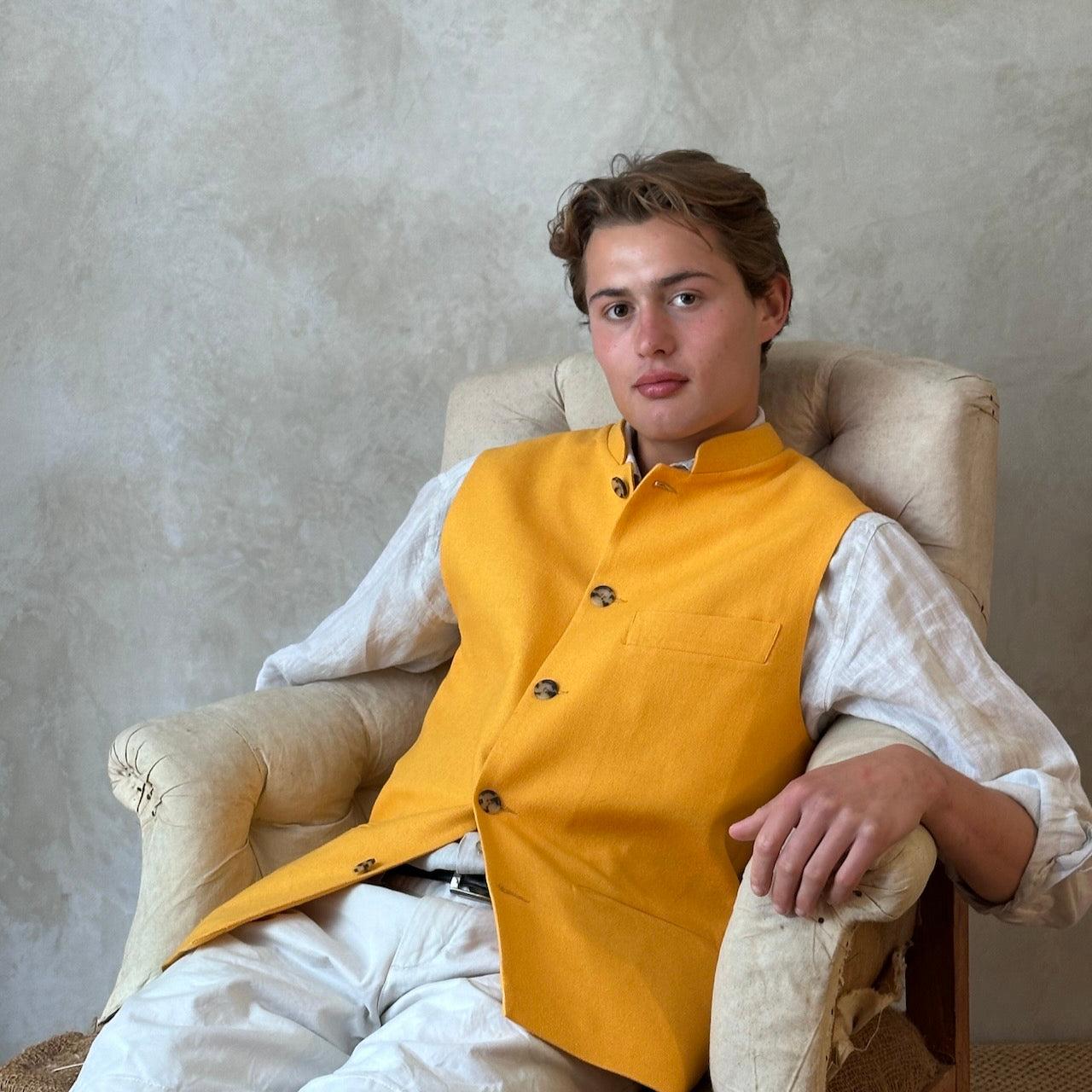 Relaxed seated view showing summer weight slim-fit gilet in bright yellow silk weave. Handmade in London this tailored cut waistcoat has a Mandarin Collar, Striped Cotton Ticking Lining and five buttons to the front. Made in Great Britain. 