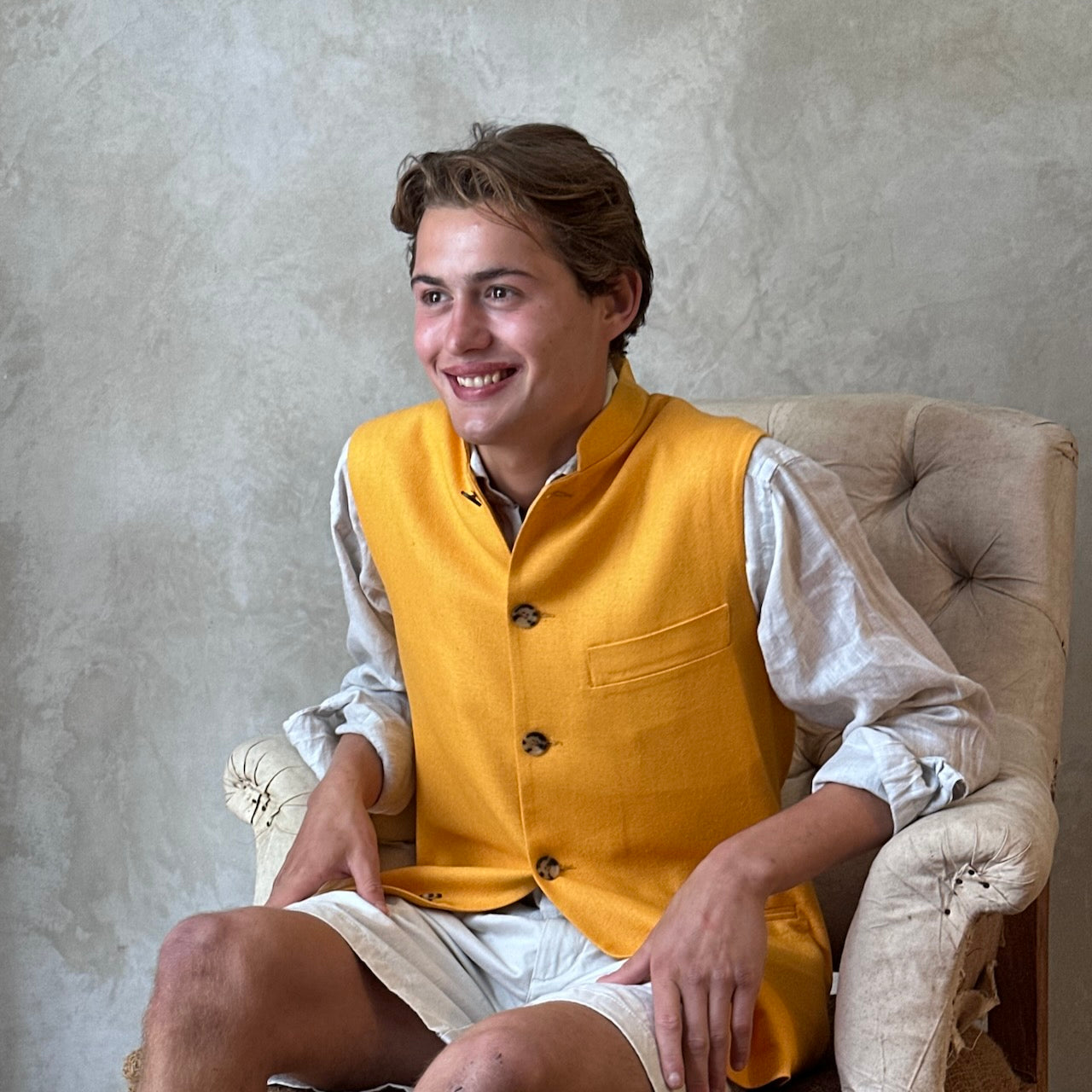 Seated view of summer weight slim-fit gilet in bright yellow silk weave. Handmade in London this tailored cut waistcoat has a Mandarin Collar, Striped Cotton Ticking Lining and five buttons to the front. Made in Great Britain. 