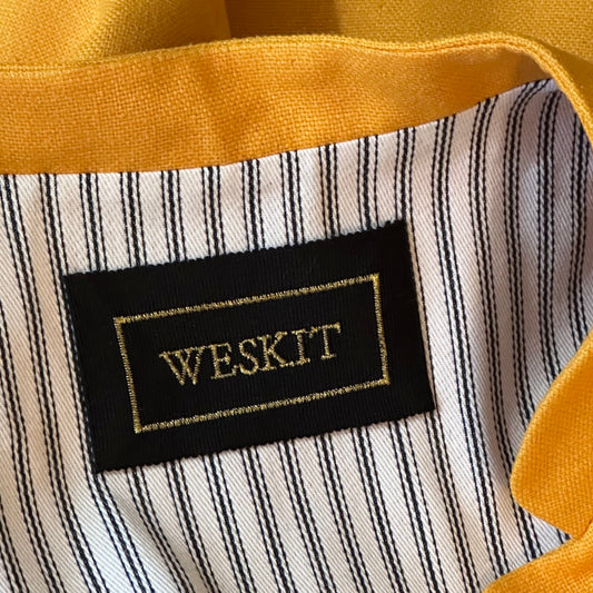 Close up on collar of summer weight slim-fit gilet in bright yellow silk weave. Handmade in London this tailored cut waistcoat has a Mandarin Collar, Striped Cotton Ticking Lining and five buttons to the front. Made in Great Britain.  Shot showing embroidered silk label and cotton ticking lining.
