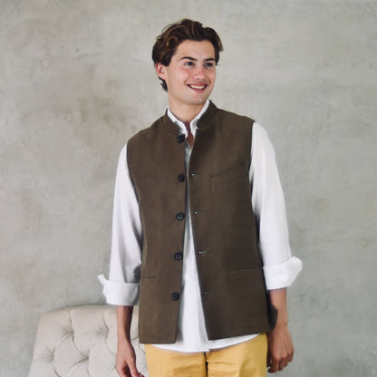 Slim Cut Nehru Style Gilet in Khaki Moleskin. This pure cotton gilet is lined in striped cotton Ticking. With a Nehru collar and five pockets it will take you everywhere and keep you warm on cooler days. Made by Hand in London. Shown unbuttoned over yellow trousers and white shirt.