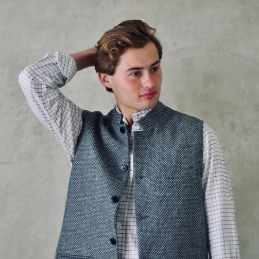 A magical limited edition mid-weight Tailored Cut waistcoat in light grey and blue tiger eye tweed. This tightly woven Yorkshire tweed has an usual patterning giving the overall effect of a mid blue from a distance, it lightens and brightens up on closer inspection as the depths and vivid colours of its patterning are revealed.
Nehru Collar, Striped Ticking lining and a Flat Horn button.
Entirely made in Great Britain.