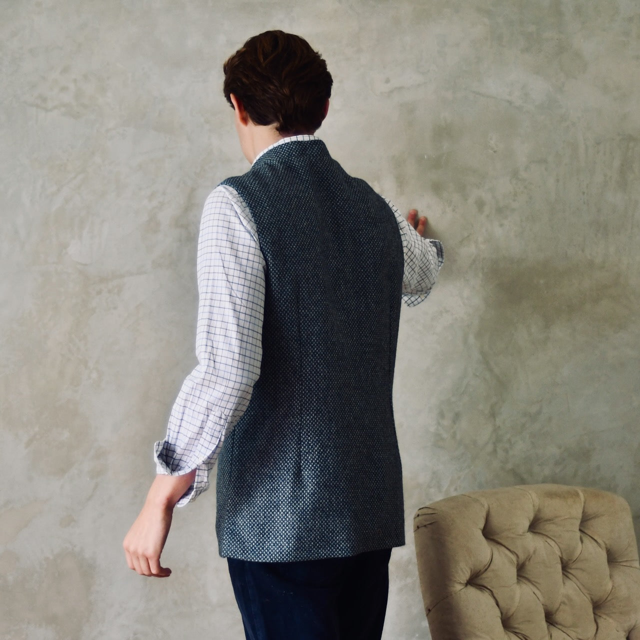 A magical limited edition mid-weight Tailored Cut waistcoat in light grey and blue tiger eye tweed. This tightly woven Yorkshire tweed has an usual patterning giving the overall effect of a mid blue from a distance, it lightens and brightens up on closer inspection as the depths and vivid colours of its patterning are revealed.
Nehru Collar, Striped Ticking lining and a Flat Horn button.
Entirely made in Great Britain. Rear View.